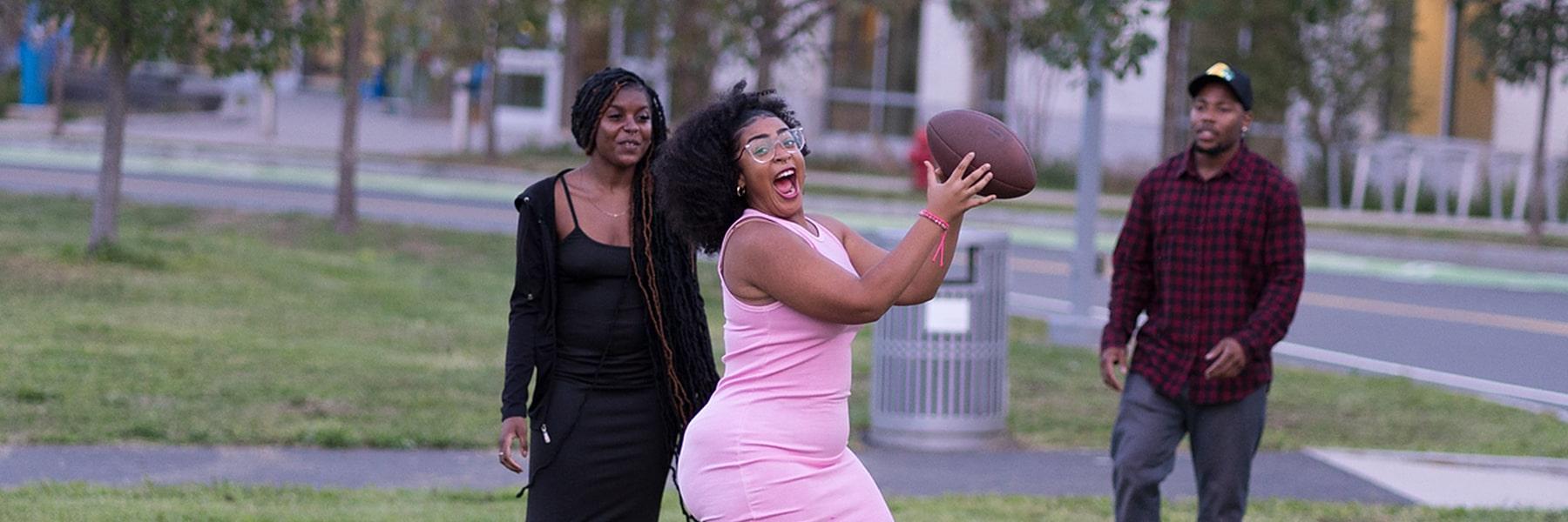 Girl in pink dress catches football at First Friday event Campus Center lawn.